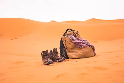 A bag and trekking shoes on the sand of the desert